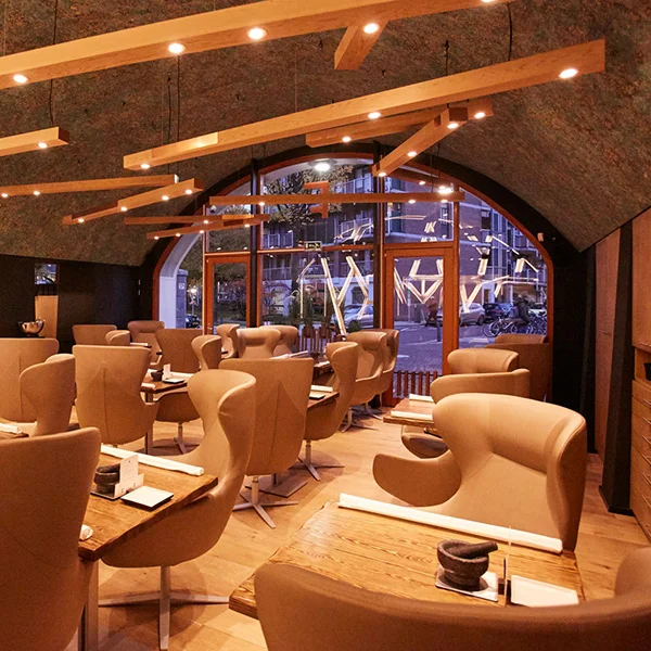 Teple osvětlená restaurace se světle hnědými křesly a závěsnými dřevěnými svítidly.