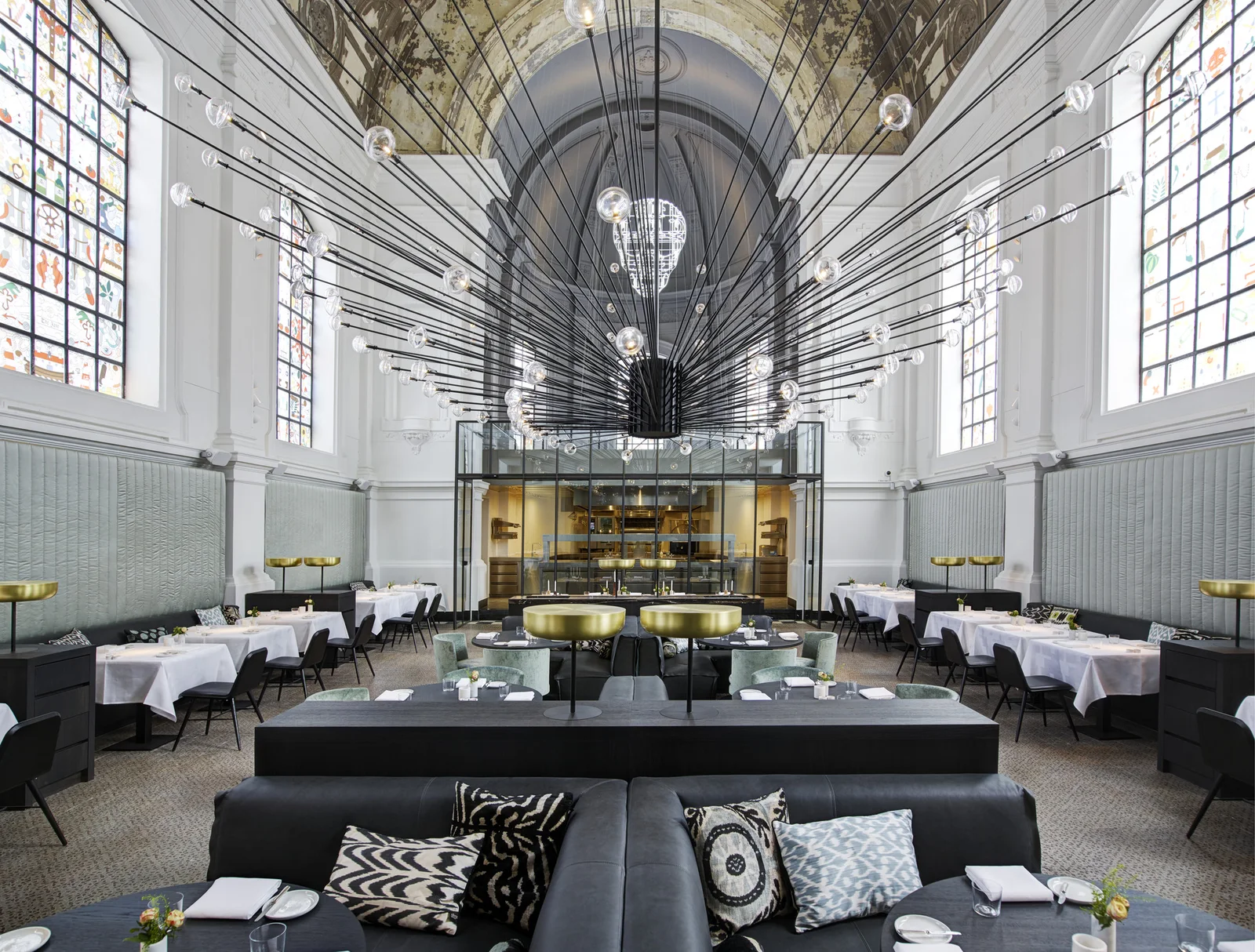 Jídelna restaurace The Jane s vitrážovými okny a velkým lustrem.